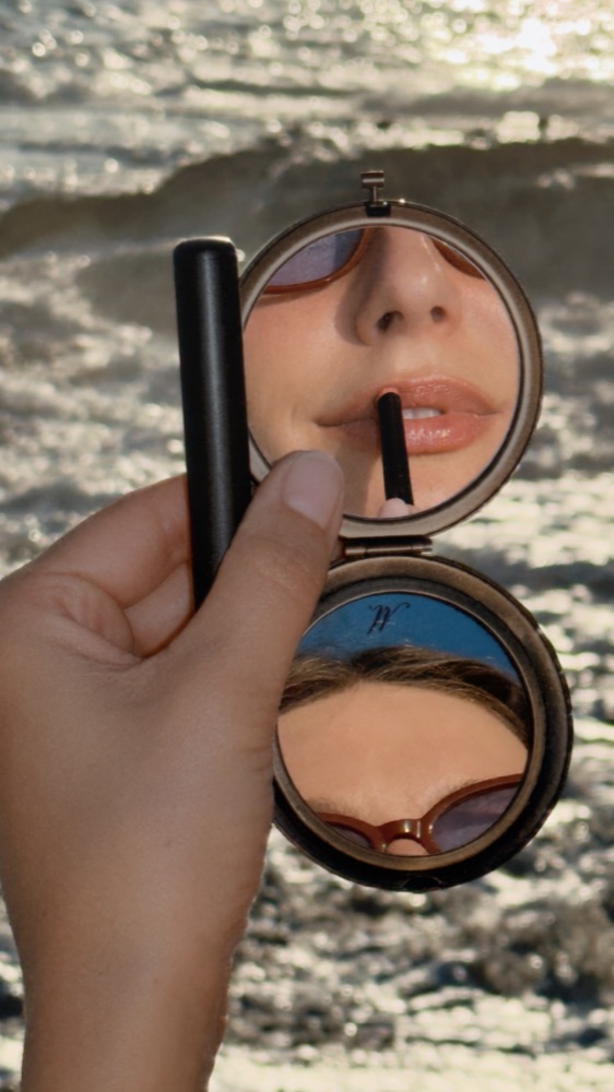 Lip liner reflected in a vintage compact mirror by the sea