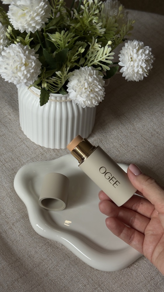 Hand holding an OGEE stick beside white flowers